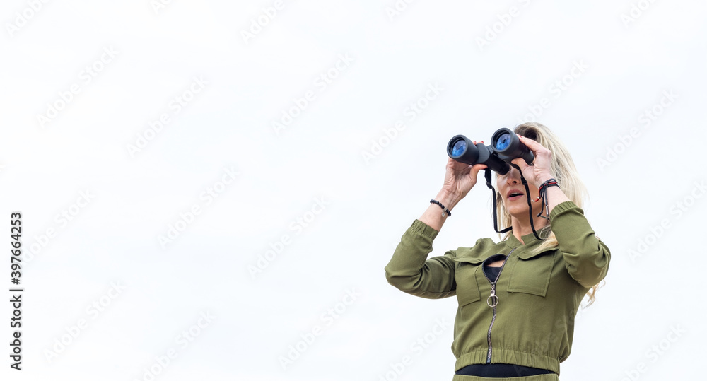 Woman looks through binoculars, standing in nature against a background of trees and sand. Woman looks through binoculars, standing in nature against a background of trees and sand.