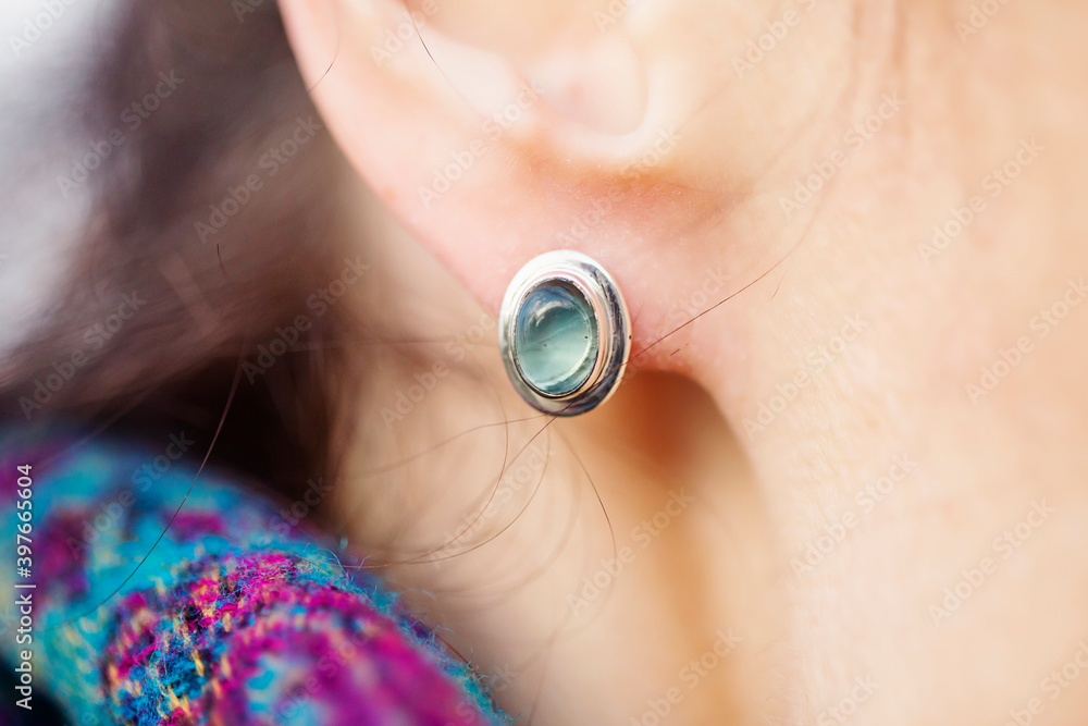 Fototapeta premium Female ear wearing elegant silver green gemstone earring