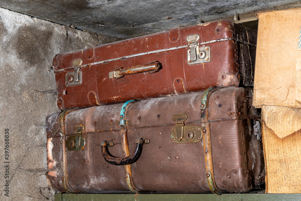 Old vintage suitcases on a shelf in abandoned garage. Corrosion on locks and handle. Dust and cobwebs on the walls.