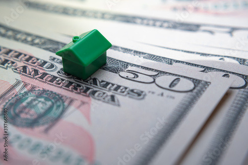 The green toy house placed on top of 50 US dollar banknotes. Macro photo. Concept image for House Price Index in the United States, first home, mortgage, real estate or house market.