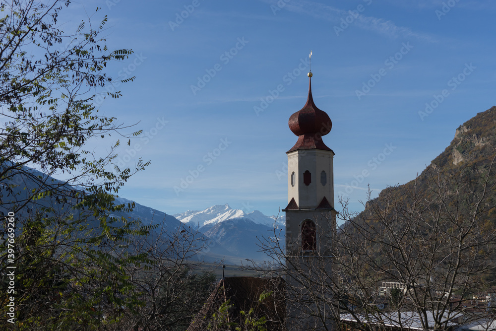 Picturesque mountain landscape in Naturns in South Tyrol in autumn, in the fore an old church and old buildings and in the background the snow-covered Alps, no people