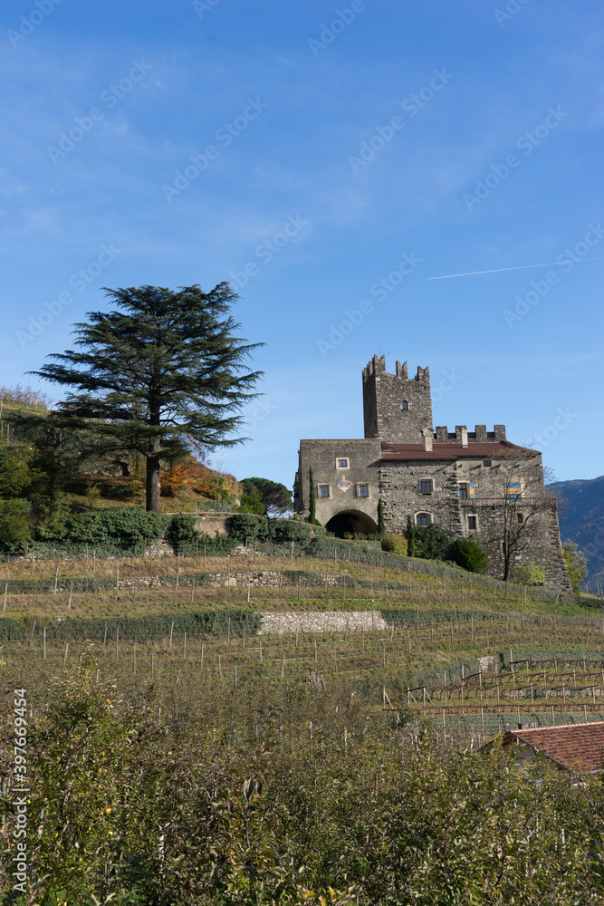 Picturesque mountain landscape in Naturns in South Tyrol in autumn, view from the hill to an old castle and the roofs of old buildings in a vineyard