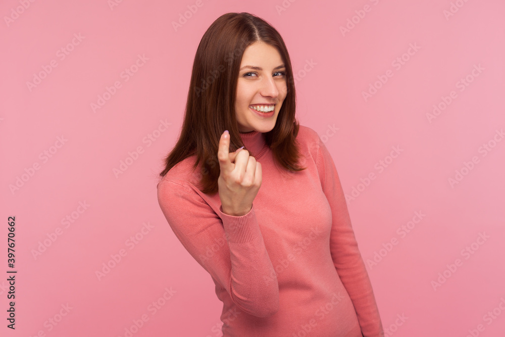Friendly positive woman with brown hair in pink sweater calling you with finger and smiling looking at camera, flirt. Indoor studio shot isolated on pink background Friendly positive woman with brown hair in pink sweater calling you with finger and smiling looking at camera, flirt. Indoor studio shot isolated on pink background