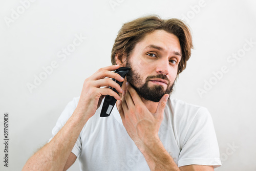 Handsome Bearded Man Trimming His Beard With a Trimmer at Morning in the Bath Room. Beauty, Hygiene, Shaving, Grooming and People Concept.