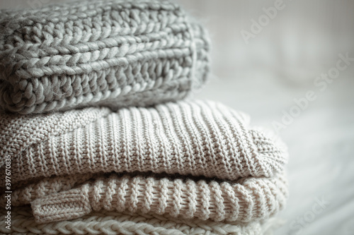 A stack of warm knitted items on blurred white background close up.