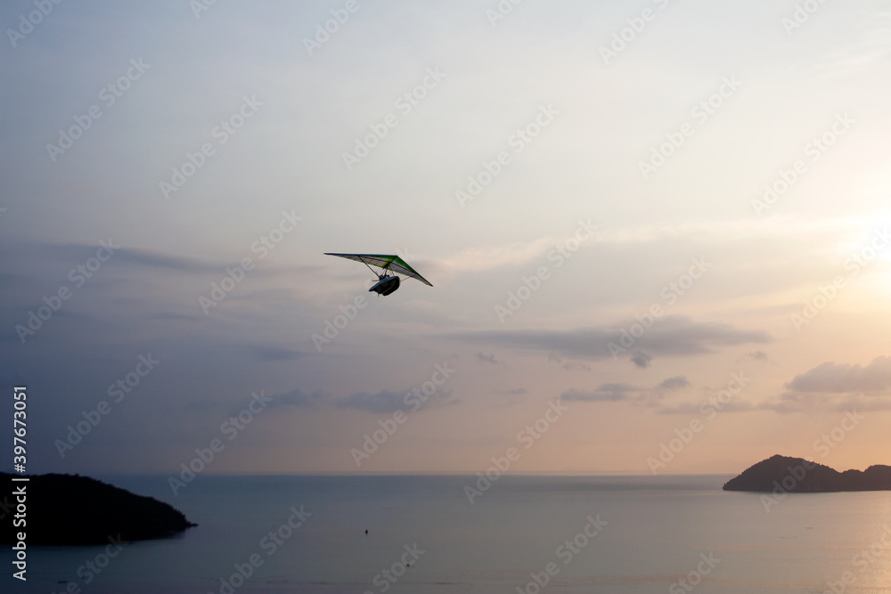 Powered water hang glider flying above sea among tropical islands during sunset