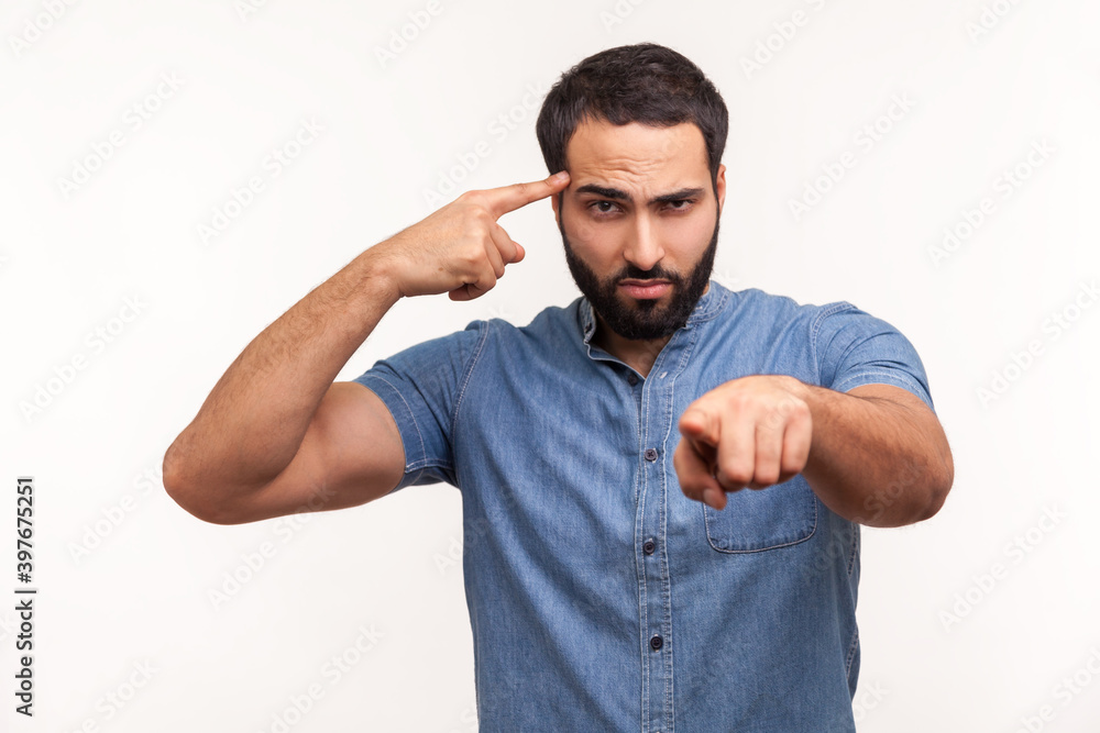Annoyed bossy man with beard twirling finger to temple pointing finger at camera, saying you are dumb and stupid, dissatisfied with dumbness. Indoor studio shot isolated on white background Annoyed bossy man with beard twirling finger to temple pointing finger at camera, saying you are dumb and stupid, dissatisfied with dumbness. Indoor studio shot isolated on white background