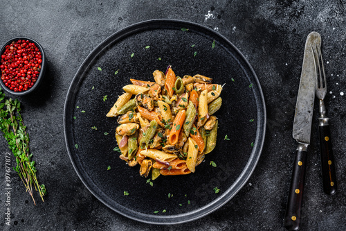 Italian Color Penne pasta with mussels on a plate. Black background. Top view