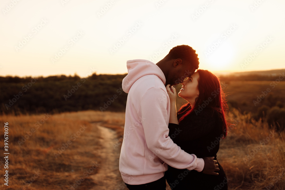 Handsome African American man gently hug beautiful white woman at sunset at the field, adorable lady smiling, enjoy tender moments, weekends outdoors, mixed race couple concept Handsome African American man gently hug beautiful white woman at sunset at the field, adorable lady smiling, enjoy tender moments, weekends outdoors, mixed race couple concept