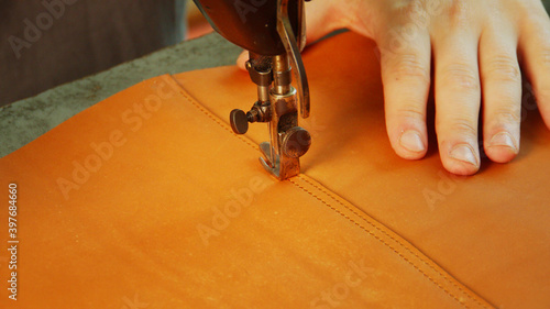 Slow-motion video a sewing machine makes a stitch with a thread on a leather bag. Close-up of the tailor's hand.