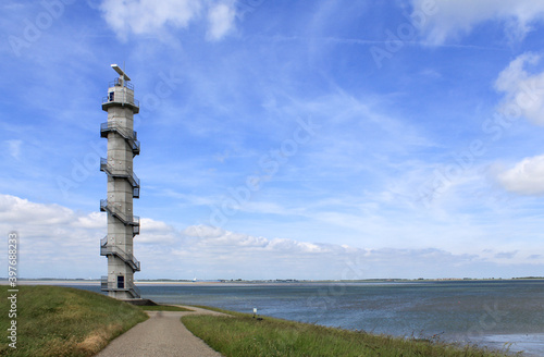 a radar tower at the seawall of the westerschelde sea in zeeland, the netherlands in springtime and a blue sky and water in the background © Angelique
