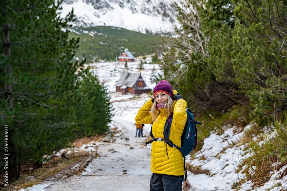 Smiling blond woman hiker in a yellow down jacket with a backpack spends his free time in the beautiful mountains.