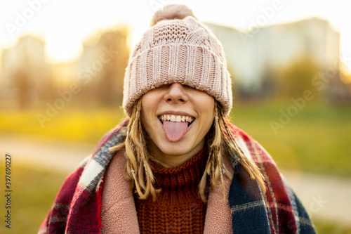 Playful woman covering eyes with knit hat sticking out tongue 