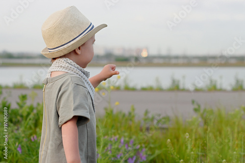 Stylish, happy child walks in the summer park by the river in a straw hat