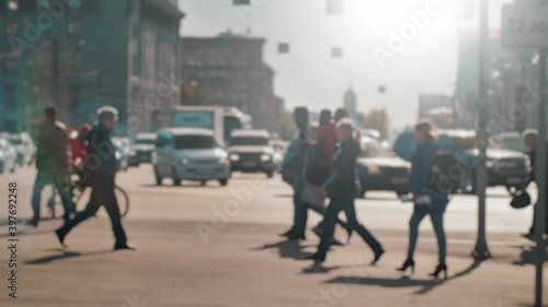 Lens blur, out of focus. A crowd of people is walking along the pedestrian crossing against the background of passing cars. People are walking around the big city. Slow motion.