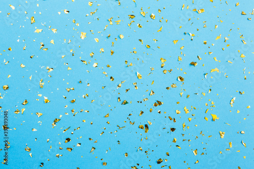 Gold confetti on blue paper background. Festive holiday backdrop. Birthday congratulations Christmas New Year. Flat lay, top view, copy space.