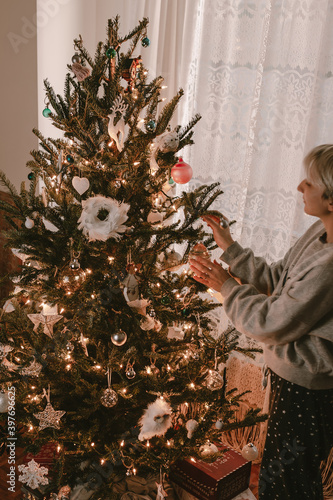 Young woman decorates Christmas tree. Holiday season. Lights, ornaments, vintage retro decor. Green fur tree. Merry Christmas, Happy New Year.Holiday is over. Pack stuff to the boxes. Red, green,white photo