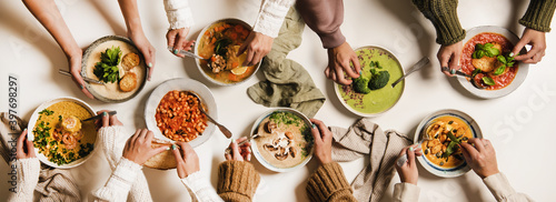 People eating Autumn and Winter creamy vegan soups, fall and winter vegetarian food menu. Flat-lay of peoples hands with homemade soup in plates and bread slices over white table background, top view