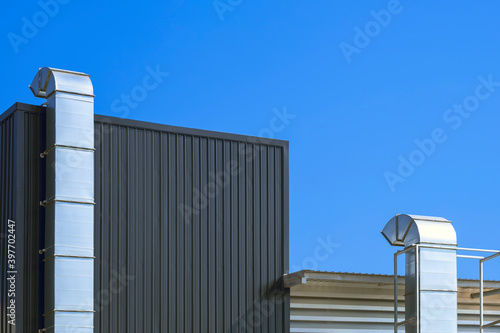 Two air ventilation ducts outside of modern industrial building against blue clear sky background photo