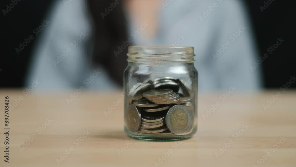 Money saving and economy Concept, Women hand hold a clear glass jar with money coin on wooden table. Close up. Money saving and economy Concept, Women hand hold a clear glass jar with money coin on wooden table. Close up.