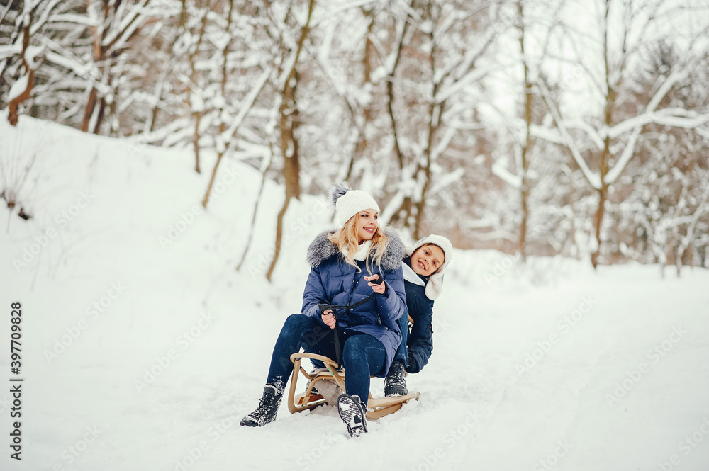 Fototapeta premium Beautiful mother in a blue jacket. Family sledding in a winter park. Little boy in a cute hat
