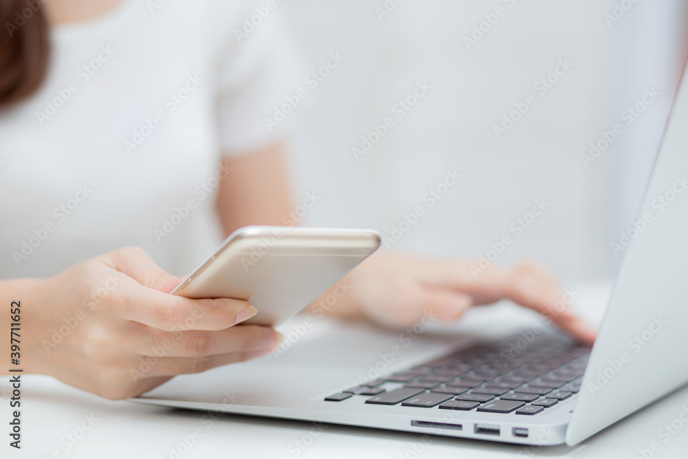 Closeup hand of young woman working laptop computer and reading smartphone on internet online on desk at home, freelance girl using phone with social media, business and communication concept. Closeup hand of young woman working laptop computer and reading smartphone on internet online on desk at home, freelance girl using phone with social media, business and communication concept.