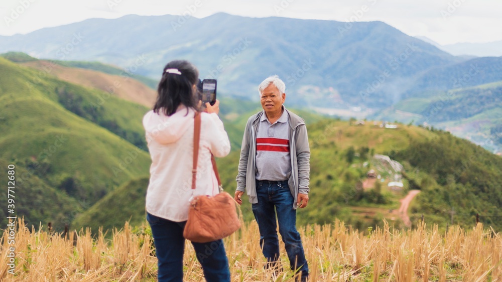 Asian old senior couples use smartphone to selfie at the top of mountain background on weekend vacation.Concept of happy living for the elderly.