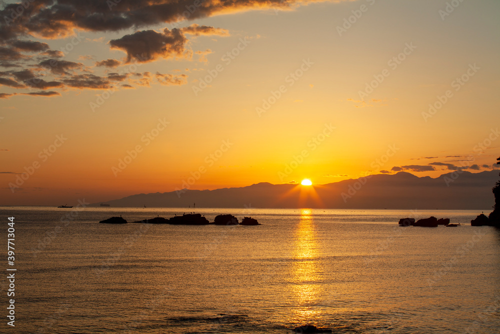 朝陽が雲と海をオレンジ色に染めて光の道をつくる
