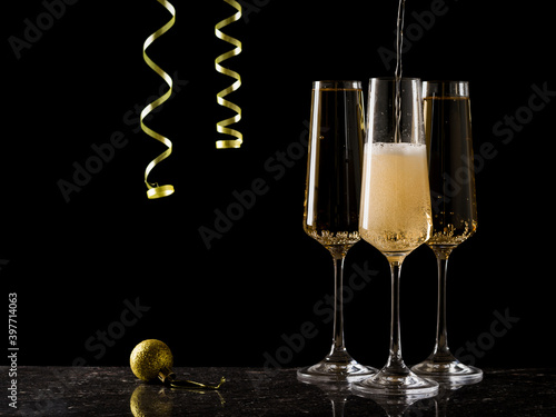 Glasses are filled with sparkling wine on a black background with a hanging serpentine.