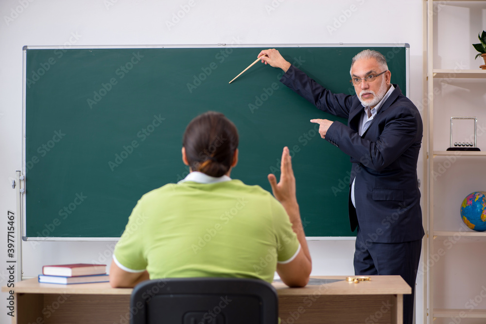 Aged teacher and young male student in the classroom Aged teacher and young male student in the classroom