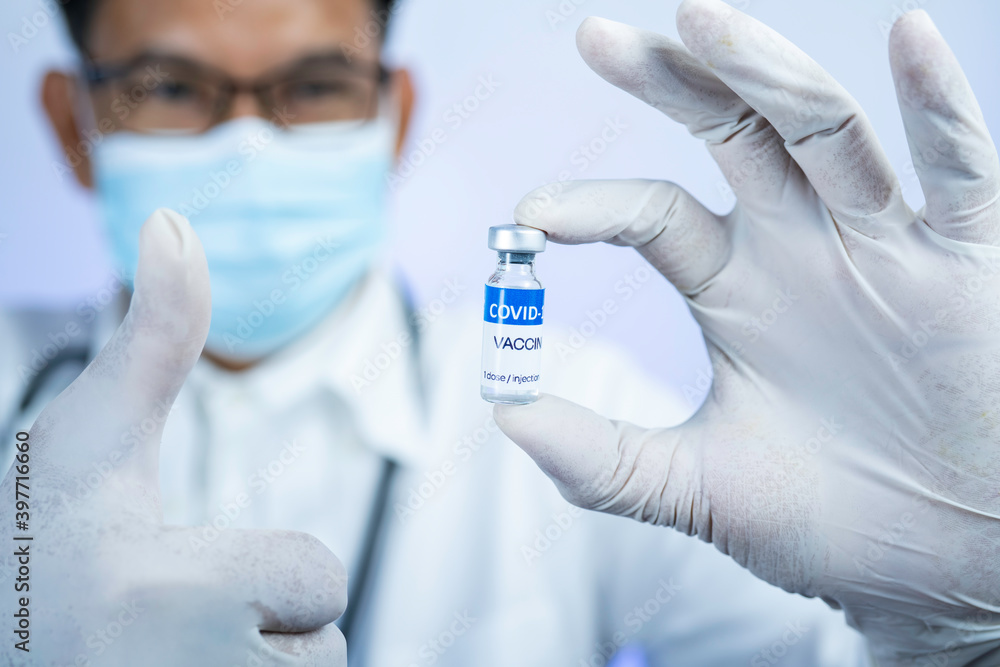 COVID-19 vaccine concept. Doctor with a stethoscope on shoulder holding COVID-19 vaccine. Covid-19 vaccine disease preparing for human clinical trials vaccination shot Selective focus. COVID-19 vaccine concept. Doctor with a stethoscope on shoulder holding COVID-19 vaccine. Covid-19 vaccine disease preparing for human clinical trials vaccination shot Selective focus.