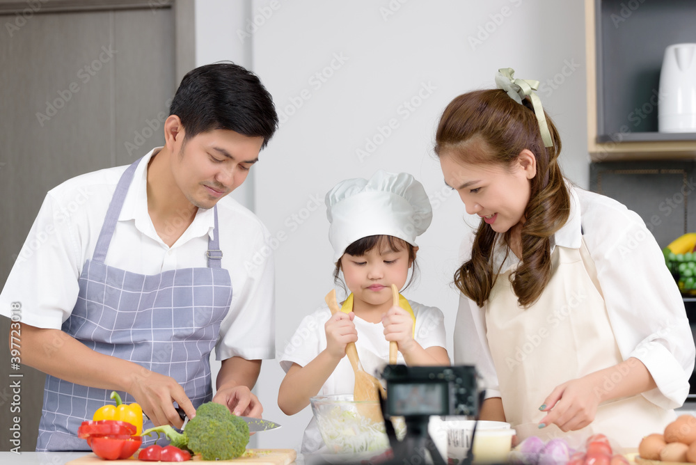 Asian family enjoys cooking together and recording video about tutorial homemade cooking at home kitchen. Person who works freelance on social media broadcasting, Activities together family.