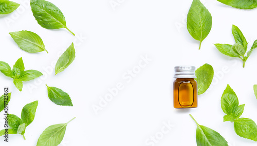 A bottle of essential oil with fresh basil leaves on white