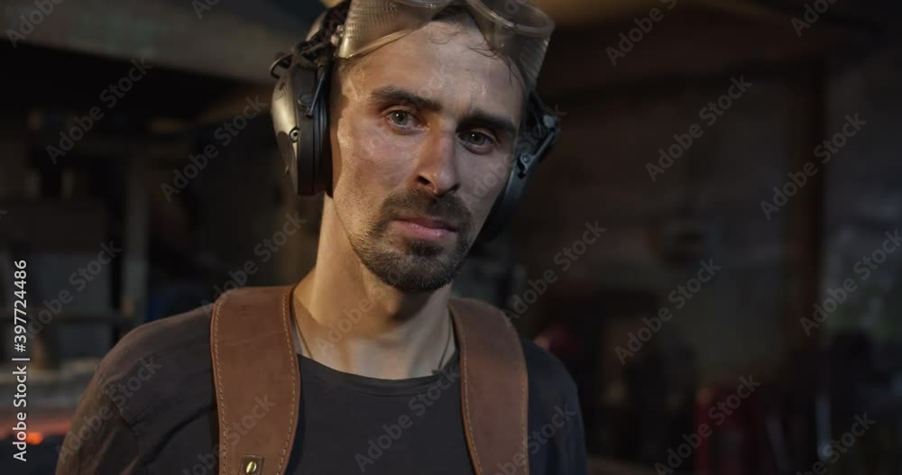 Close-up of a blacksmith, who turns to the camera, takes off his goggles and stares into the camera with smart eyes, his face drenched in sweat and soot from hard work. High quality 4k footage Close-up of a blacksmith, who turns to the camera, takes off his goggles and stares into the camera with smart eyes, his face drenched in sweat and soot from hard work. High quality 4k footage