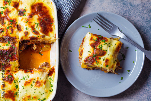 Portion of  Greek moussaka - potato and meat casserole with cheese on gray plate, dark background, top view. Greek food concept. photo