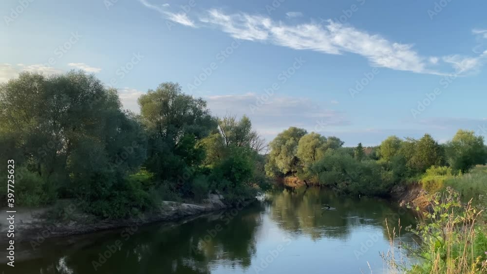The river flows slowly on a summer evening. Trees and green grass grow along the banks. The sun is shining brightly. The river flows slowly on a summer evening. Trees and green grass grow along the banks. The sun is shining brightly.