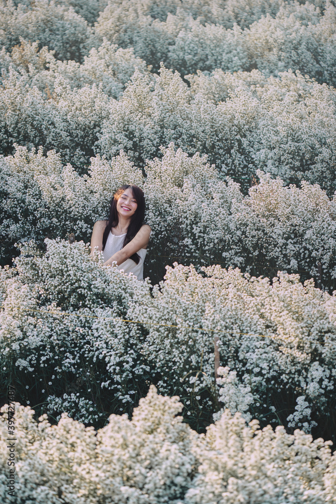 Happy Asian woman in white dress sitting in the garden of white flowers