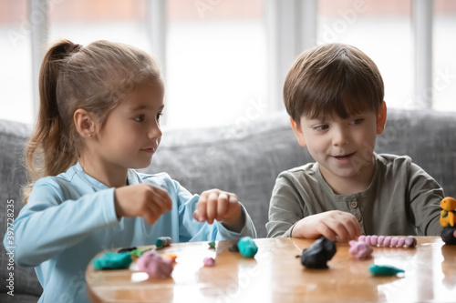 Joyful two cute little preschool children playing with colorful playdough, enjoying making handicraft plasticine figures, involved in creative handmade activity together, sitting at table indoors.