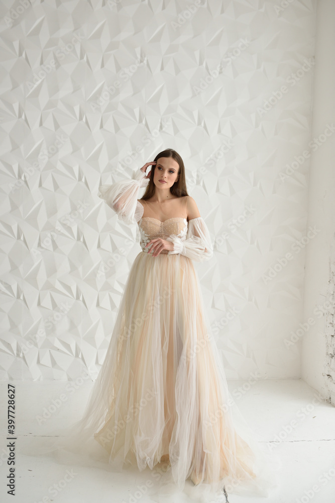 A beautiful bride in a wedding dress stands on a white studio in full growth and looks to the side A beautiful bride in a wedding dress stands on a white studio in full growth and looks to the side