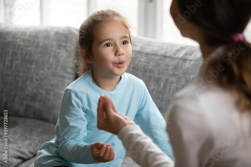 Adorable small focused 6s preschool disabled baby girl practicing correct sound pronunciation with speech therapist, making exercises at lesson, having problems or difficulties with speaking.