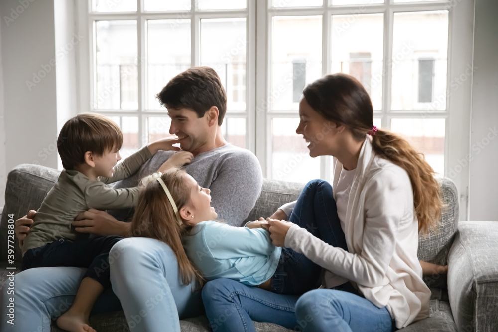 Happy family relaxing on couch, having fun tickling small cute kids siblings. Joyful couple parents holding on laps little son and daughter, playing together in living room, leisure activity concept. Happy family relaxing on couch, having fun tickling small cute kids siblings. Joyful couple parents holding on laps little son and daughter, playing together in living room, leisure activity concept.