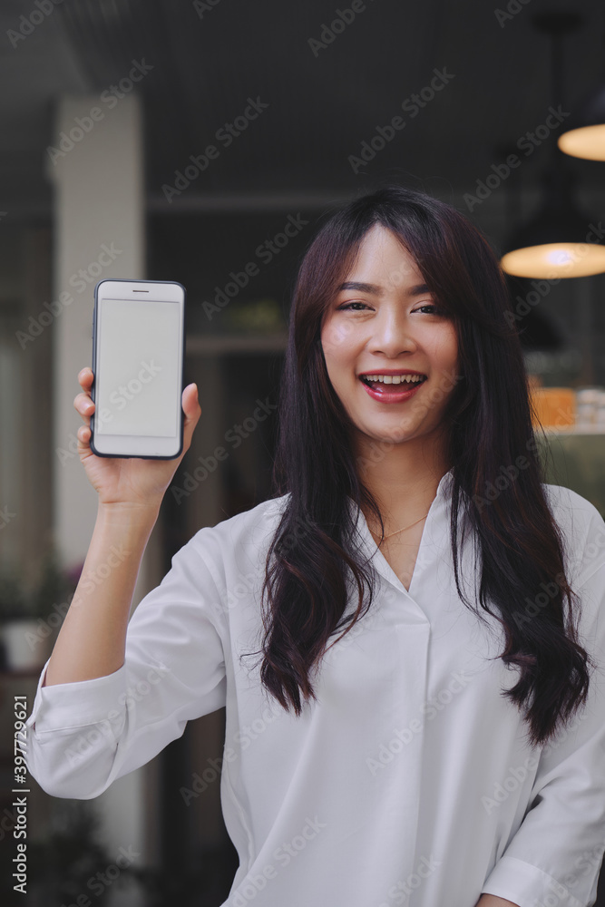 young attractive Asian woman showing her smartphone with white screen to the camera in a coffee shop mockup phone screen
