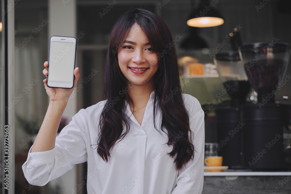 young attractive Asian woman showing her smartphone with white screen to the camera in a coffee shop mockup phone screen