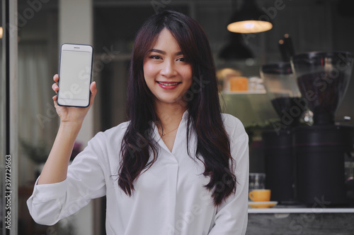 Obraz na płótnie young attractive Asian woman showing her smartphone with white screen to the camera in a coffee shop mockup phone screen w salonie
