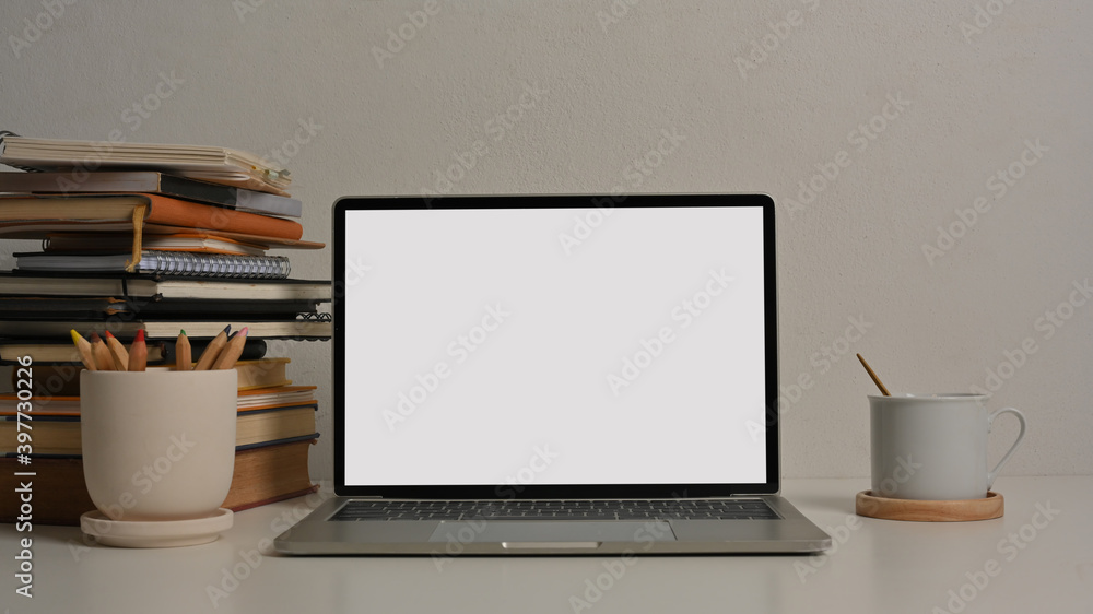 Study table with laptop, stack of books, stationery and cup in home office room Study table with laptop, stack of books, stationery and cup in home office room