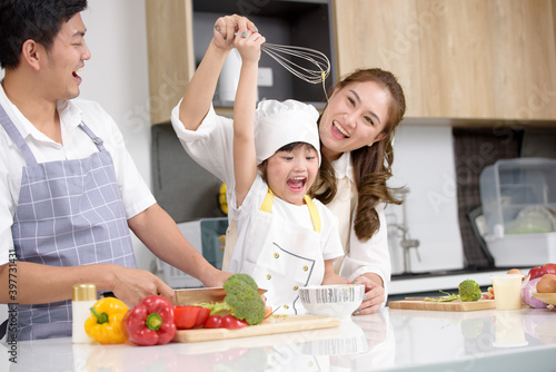 Asian family smashes egg into the bowl and daughter whisking eggs in bowl on white table, Happy to cooking food with her mom and dad in the home kitchen while her mother teaches photo