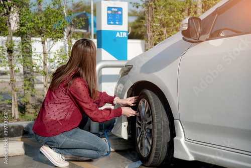 An Asian Woman inflates tires at a gas station And he is looking at the dial of the auto inflator to check the pressure level.