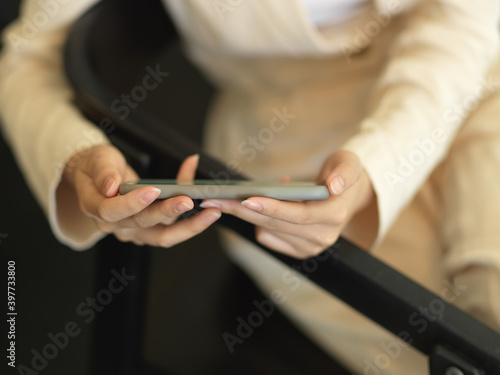 Female hands holding horizontal smartphone while sitting on armchair