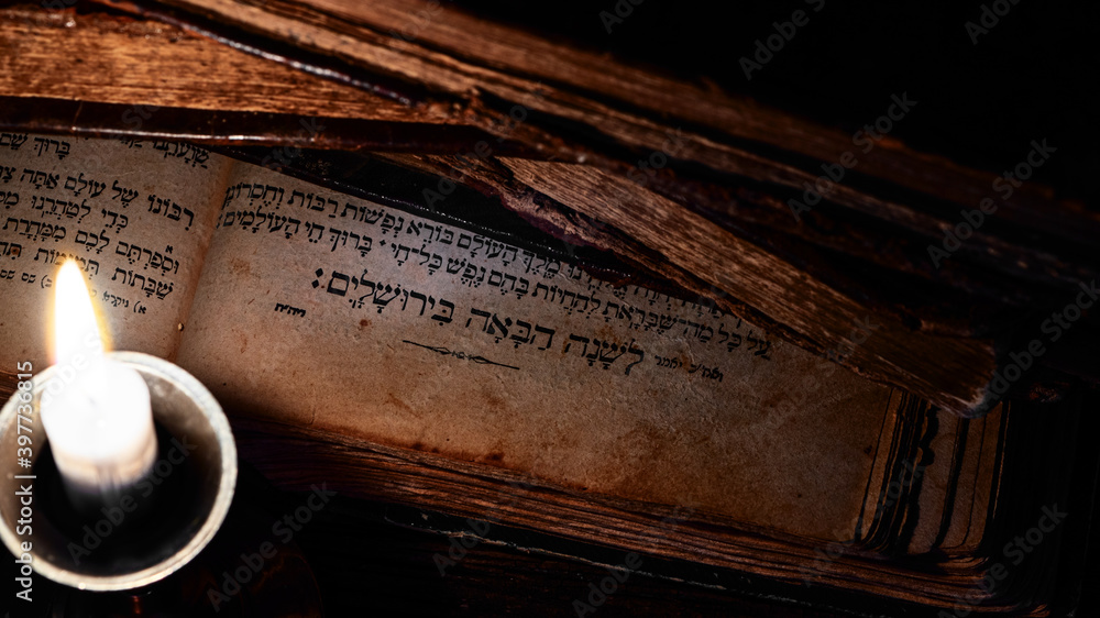 Old jewish books on open page of Makhzor with Jewish prayer L'Shana Haba'ah B'Yerushalayim which translates as Next year in Jerusalem and burning candle. Concept of return to a rebuilt Jerusalem.