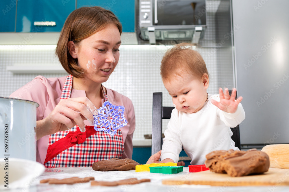 Fototapeta premium A young caucasian mother makes cookies with her baby. Close-up portrait. Kitchen in the background. The concept of home-made food and cooking with children